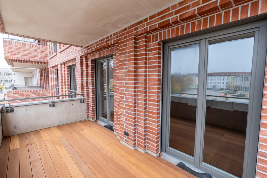 Neubauwohnung: Balkon mit Holzboden, Backsteinmauer und Fenster. 2-Raum-Wohnung.