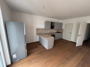 Moderne Einbauküche mit grauen Fronten, Holzoptik-Arbeitsplatte und großem Kühlschrank in 2-Raum-Wohnung.
