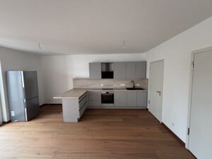 L-förmige Einbauküche mit grauen Fronten, Holz-Arbeitsplatte, Herd und Kühlschrank in einer 2-Raum-Wohnung.
