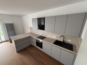 Offene Einbauküche mit grauen Fronten, dunkler Armatur, Induktionsherd und Holzoptik-Arbeitsplatte in 2-Raum-Wohnung